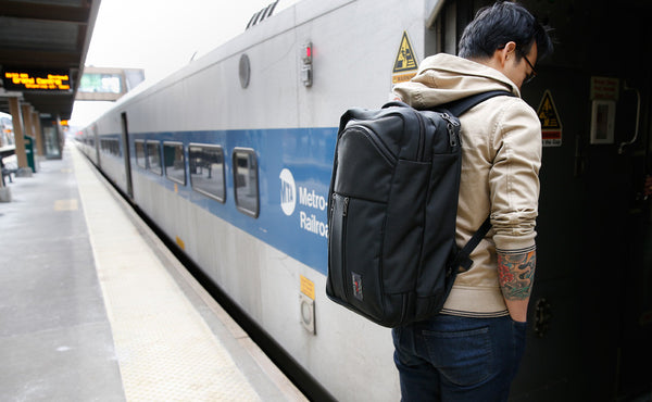 A person entering a rail car while carrying a Black 525 Ballistic Western Flyer using the included backpack straps.